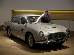 FILE - In this Tuesday, June 19, 2018 file photo, a staff member from the Bonhams motor car department poses for photographers with the 1965 Aston Martin DB5 driven by actor Pierce Brosnan in his role as James Bond in the 1995 movie GoldenEye during a photocall at premises of Bonhams auction house in London. Aston Martin, the maker of James Bond's favorite sports car, says it may sell shares for the first time as the company seeks to attract more wealthy buyers with an expanded product range including sedans, sports utility vehicles and even submarines.