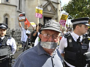 A supporter of Tommy Robinson in the foreground poses for a photo as Stand Up to Racism demonstrators protest outside the Royal Courts of Justice, in London, Wednesday, Aug. 1, 2018.  A British court has ordered prominent far-right activist Tommy Robinson to be released on bail while he appeals a finding of contempt of court. Robinson had been jailed for 13 months after live-streaming outside a criminal trial in violation of reporting restrictions. Court.