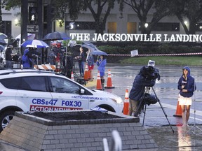 Members of the media are sheltered from the rain as they do their early morning broadcasts across the street from the Jacksonville Landing following the mass shooting that occurred there Sunday in downtown Jacksonville, Fla., Monday, Aug. 27, 2018.