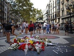 A woman places a flower around a memorial tribute of flowers, messages and candles on Barcelona's historic Las Ramblas in Barcelona, Thursday, Aug. 16, 2018, the day before to the anniversary of the attacks that took place here on Aug. 17, 2017 killing 16 people and injuring more than 120.