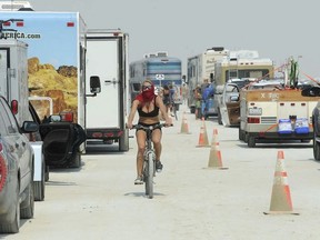File - In this Aug. 26, 2013 file photo, a woman rides her bike between cars waiting to enter Burning Man in Gerlach, Nev. Burning Man organizers are threatening to sue federal officials over a dramatic increase in traffic stops of vehicles bound for the annual counter-culture festival in the Nevada desert 100 miles (160 kilometers) north of Reno. The Reno Gazette Journal reported Friday, Aug. 24, 2018, the organization's lawyer sent a letter to the U.S. Bureau of Indian Affairs calling for an immediate halt to the "unconstitutional" tactic.