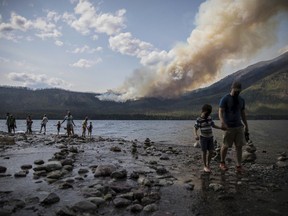 FILE - In this Sunday, Aug. 12, 2018 file photo provided by the National Park Service, people walk along the shore near Lake McDonald Lodge as the Howe Ridge Fire burns in Glacier National Park, Mont. Wildfires that have kept portions of Glacier National Park closed for two weeks are scrambling visitors' plans and prompting some to cancel their trips. Much of Glacier's famous Going-to-the-Sun-Road has been closed since August 12 due to a fire that's burned more than 19 square miles (50 square kilometers). (National Park Service via AP, File)