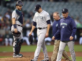 Seattle Mariners pitcher James Paxton, second from left, is escorted off the field after being hit by a ball in the first inning of a baseball game against the Oakland Athletics Tuesday, Aug. 14, 2018, in Oakland, Calif.