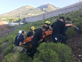 In this Saturday, Aug. 4, 2018 photo, firefighters with the Flagstaff Fire Department carry a man who was caught in a storm drain in Flagstaff, Ariz. Officials believe the man crawled into the drain and fell through a series of drainage tubes.