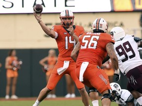 Oklahoma state quarterback Taylor Cornelius (14) throws a pass over teammate and offensive lineman Larry Williams (56) while under pressure from Missouri State defensive tackle Kylin Washington (99) during the first quarter of an NCAA college football game in Stillwater, Okla., Thursday, Aug. 30, 2018.