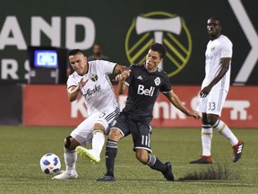 Vancouver Whitecaps' David Guzman (20) vies with Portland Timbers Nicolas Mezquida (11) for possession of the ball during an MLS soccer match Saturday, Aug. 11, 2018, in Portland, Ore.