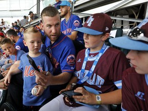 New York Mets' Todd Frazier, second from left, holds his son Blake as he asks Coventry, Rhode Island players Paulie Manfredo, second from right, and Aiden Wilkins, right, to help him send a message from his phone while taking in a baseball game in International pool play at the Little League World Series tournament in South Williamsport, Pa., Sunday, Aug. 19, 2018. The Mets will be playing the Philadelphia Phillies in the Little League Classic in Bowman Stadium in Williamsport, Pa., on Sunday Night Baseball.