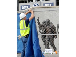 FILE - In this Sunday, July 22, 2012 file photo, a worker hangs a blue tarp over a fence that was installed around the Joe Paterno statue as crews worked to remove the statue in State College, Pa. The university removed the monument in the wake of an investigative report that found that the late coach and three other top Penn State administrators concealed sex abuse claims against Jerry Sandusky, who was convicted of sexually abusing 10 boys, sometimes on Penn State's campus.