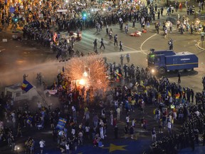 In this Friday, Aug. 10, 2018, photo, a teargas canister explodes as riot police charge using canon to clear the square during protests outside the government headquarters in Bucharest, Romania. Romanian authorities say hundreds of people including two dozen riot police have received medical treatment after an anti-government protest turned violent and two weapons were stolen from riot police officers.