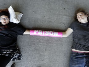 Ben Foster, left, and Kaitlyn Brock lie on the ground as they block an entrance to a parking garage outside the headquarters of CoreCivic Monday, Aug. 6, 2018, in Nashville, Tenn. The Tennessee-based company is one of the nation's largest private prison operators and also runs eight immigration detention centers for Immigration and Customs Enforcement.