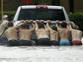 FILE - In this Aug. 27, 2017 file photo, people push a stalled pickup to through a flooded street in Houston, Texas after Tropical Storm Harvey dumped heavy rains. Hurricane Harvey roared onto the Texas shore nearly a year ago, but it was a slow, rainy roll that made it a monster storm. Federal statistics show some parts of the state got more than 5 feet of rain in five days. Harvey killed dozens and swamped a section of the Gulf Coast that includes Houston, the nation's fourth largest city, causing billions of dollars in damage.