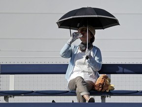 A fan shelters under an umbrella and sips a drink as she watches the match between Fabio Fognini, of Italy, and Michael Mmoh during the first round of the U.S. Open tennis tournament, Tuesday, Aug. 28, 2018, in New York.