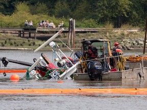 Workers watch as a capsized tugboat is lifted from the Fraser river between Vancouver and Richmond, B.C., on Wednesday, August 15, 2018.