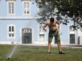 A man walks under the water from a garden sprinkler by the Tagus riverbank in Lisbon, Thursday, Aug. 2 2018. The temperature in Lisbon reached 39 degrees Celsius, 102.2 Fahrenheit, on Thursday and is expected to keep rising over the next few days.