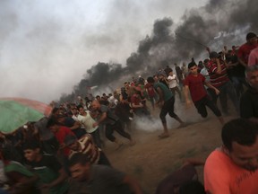 Protesters run to cover from teargas fired by Israeli troops, while others burn tires near fence of the Gaza Strip border with Israel, during a protest east of Gaza City, Friday, Aug. 31, 2018. Gaza's Health Ministry says Israeli gunfire wounded about 80 Palestinians at a weekly protest along the border with Israel.