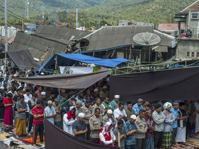Muslim men perform Friday prayer as houses ruined by Sunday's earthquake are seen in the background at a makeshift mosque in Pamenang, Lombok Island, Indonesia, Friday, Aug. 10, 2018. The north of the popular resort island has been devastated by Sunday's earthquake, damaging thousands of buildings and killing a large number of people.