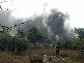 In this Tuesday, July 31, 2018 photo provided by Alberto Herrera, a survivor stands in a rain shower in a field watching smoke billow from the downed Aeromexico jetliner he was traveling in, near the airport in Durango, Mexico. Authorities in Mexico said there were no fatalities among the 97 passengers and four crew members aboard the Embraer 190 jet that crashed moments after takeoff in Durango, sending plumes of black and gray smoke into the sky. Rescuers took 49 people to hospitals; most of them had minor injuries.