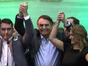 FILE - In this July 22, 2018 file photo, Brazil's presidential candidate Jair Bolsonaro, center, holds hands with his wife Michelle and son Flavio before supporters during the National Social Liberal Party convention where he accepted the party's nomination in Rio de Janeiro, Brazil. The far-right presidential candidate announced on Sunday, Aug. 5, 2018 that he has picked Army Reserve General Hamilton Mourao as his running mate for Brazil's upcoming general elections in October.
