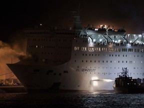 A firefighting vessel throws water as smoke rises from the Eleftherios Venizelos ship at the port of Piraeus, near Athen Wednesday, Aug. 29 2018. The passenger ferry with hundreds of passengers and crew arrived early Wednesday at the port of Piraeus after a fire broke out while the vessel was en route to the island of Crete, Greek coast guard said.