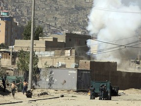 Smoke rises from a house where suspected attackers were hiding while policemen arrests two suspects, left, in Kabul, Afghanistan, Tuesday, Aug. 21, 2018. The Taliban fired rockets toward the presidential palace in Kabul Tuesday as President Ashraf Ghani was giving his holiday message for the Muslim celebrations of Eid al-Adha, said police official Jan Agha.