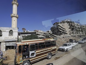 In a picture taken through a bus window, people drive their cars in Damascus, Syria, Monday, Aug. 13, 2018. Syrian government officials vowed Monday to ensure the safe return of refugees and urged Western countries to encourage the process by lifting sanctions. Public Administration Minister Hussein Makhlouf said authorities are working to rebuild hospitals, schools and other infrastructure to help accommodate refugees.