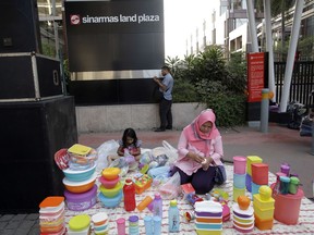 In this Aug. 5, 2018, photo, a mother sells food and beverage containers in front of building that houses the headquarters of Sinarmas Group, one of Indonesia's largest palm oil company, in Jakarta, Indonesia. The main global group for certifying sustainable wood has suspended plans to give its influential endorsement to Indonesian paper giant Sinarmas after revelations it cut down tropical forests and used an opaque corporate structure to hide its activities.