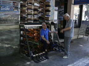 Two men talk at the entrance of a shop selling shoes in central Athens, Monday, Aug. 20, 2018, on the day that Greece's eight-year crisis will be officially over.  But few Greeks see cause for celebration, though the economy is once again growing modestly and state finances are improving, exports are up and unemployment is down from a ghastly 28 percent high.