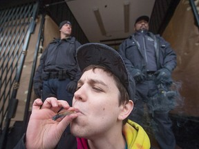 A young man smokes a joint as police officers stand outside the Cannabis Culture shop during a police raid, in Vancouver, B.C., on Thursday March 9, 2017.