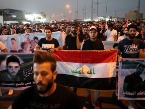 FILE - In this Sept. 11, 2018 file photo, demonstrators hold national flags and posters of protesters who were killed during previous demonstrations, in Basra, Iraq. A police official said Tuesday, Sept. 25, 2018, that masked gunmen shot dead Soad al-Ali, a human rights activist, who has been involved in organizing protests demanding better services in the city, and a mother of four, outside a supermarket in Basra.