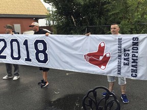 In this Tuesday, Sept. 18, 2018 photo, friends hold a banner they found in Somerville, Mass., that proclaims the Boston Red Sox are the 2018 American League East Champions, though the team has not yet clinch the division. A Red Sox spokesman said the banner apparently fell off a vendor's delivery truck, and planned to send a courier to retrieve the banner Wednesday.
