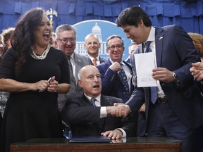 State Sen. Kevin de Leon, D-Los Angeles, right, shakes hands with Gov. Jerry Brown after Brown signed his environmental measure SB100, Monday, Sept. 10, 2018, in Sacramento, Calif. SB100 sets a goal of phasing out all fossil fuels from the state's electricity sector by 2045. Assemblywoman Lorena Gonzalez Fletcher, D-San Diego, left, who carried the bill in the Assembly, reacts.