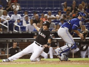 Miami Marlins' J.T. Realmuto, left, slides into home to score during the fifth inning of a baseball game against Toronto Blue Jays catcher Danny Jansen, Friday, Aug. 31, 2018, in Miami.