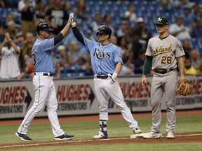 Tampa Bay Rays third base coach Matt Quatraro (33) congratulates Brandon Lowe, center, after his triple during the seventh inning of a baseball game against the Oakland Athletics, Sunday, Sept. 16, 2018, in St. Petersburg, Fla.