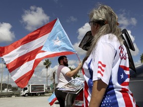 Aaron and Diana Umpirerre gather in the parking lot to meet others to head to West Palm Beach for a protest, Saturday, Sept. 22, 2018 in Hollywood, Fla.  Activists marking the one-year anniversary of Hurricane Maria's devastation of Puerto Rico are staging a rally and caravan focused on President Donald Trump's Mar-a-Lago resort in Florida.