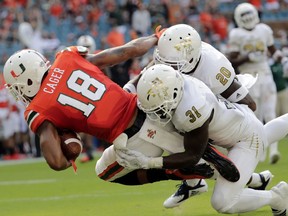 Miami wide receiver Lawrence Cager (18) scores a touchdown as FIU defensive back Tyree Johnson (31) and defensive back Emmanuel Lubin (20) defend during the first half of an NCAA college football game, Saturday, Sept. 22, 2018, in Miami Gardens, Fla.