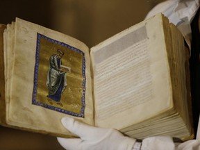 A Greek conservator holds up a repatriated 12th Century illuminated manuscript bible, during its presentation at the Byzantine Museum in Athens, Monday, Sept. 15, 2014.