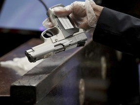 In this Tuesday Sept. 18, 2018 photo, Chicago Police Detective Roberto Garcia holds officer Jason Van Dyke's 9mm semiautomatic Smith and Wesson at the trial for the shooting death of Laquan McDonald at the Leighton Criminal Court Building in Chicago. Garcia was asked to confirm it was the gun Van Dyke turned in hours after the shooting that Van Dyke used to kill McDonald.