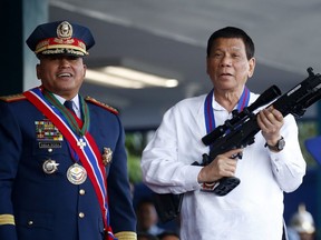 In this April 19, 2018 file photo, Philippine President Rodrigo Duterte, right, jokes to photographers as he holds an Israeli-made Galil rifle which was presented to him by former Philippine National Police Chief Director General Ronald "Bato" Dela Rosa at the turnover-of-command ceremony at the Camp Crame in Quezon city northeast of Manila.