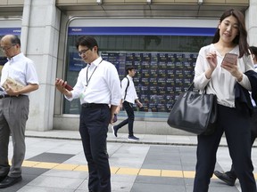 In this Sept. 11, 2018, photo, people use smartphones in front of an electronic stock board of a securities firm in Tokyo. Asian shares were mostly higher Wednesday, Sept. 19, 2018, despite jitters over the escalating trade dispute between the U.S. and China.