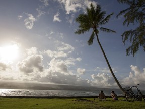 FILE - In this Aug. 30, 2015, file photo, Keenin Ide, left, of Hilo, Hawaii, and Medea Yankova, of Sofia, Bulgaria, sit near Hilo Bay in Hilo, Hawaii. The Big Island visitors bureau and Hawaii County have launched a campaign that aims to create a more conscientious tourism industry on the Big Island. The Island of Hawaii Visitors Bureau Executive Director Ross Birch and county Managing Director Will Okabe presented the new "Pono Pledge" at a Thursday, Sept. 20, 2018, event, the Hawaii Tribune-Herald reported.