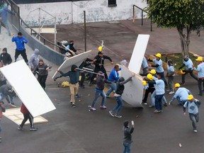 In this photo provided by the Andina government news agency, Alianza Lima club soccer fans, left, fight with members of an evangelical church, yellow helmets at right, outside the soccer club's stadium in Lima, Peru, Monday, Sept. 10, 2018. The two groups clashed outside the stadium over who has the right to use the area surrounding the sports venue, after the religious group arrived early in the morning and started removing the team's logos from the parking area.