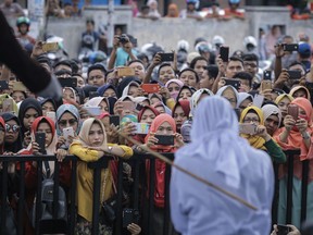People use their mobile phones to take pictures as a Shariah law official whips a woman who is convicted of prostitution during a public caning outside a mosque in Banda Aceh, Indonesia, Friday, April 20, 2018.