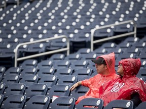 Fans sit in the rain before a baseball game between the Washington Nationals and the New York Mets at Nationals Park, Sunday, Sept. 23, 2018, in Washington.