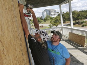 FILE - In this Wednesday, Sept. 12, 2018 file photo, Joe Gore, left, and Joshua Adcock prepare for Hurricane Florence as they board up windows on a home in Emerald Isle N.C. Before and after a hurricane, Ace is the place. And Home Depot, Lowe's, and many other hardware and building supply outlets. Not surprisingly, these companies plan for storms such as Hurricane Florence all year.
