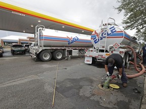 FILE- In this Sept. 17, 2018, file photo people wait in line as Travis Hall, right, and Brandon Deese, back, pump fuel from two tanker trucks at a convenience store in Wilmington, N.C.  America's rediscovered prowess in oil production is shaking up old notions about the impact of higher crude prices on the U.S. economy.
