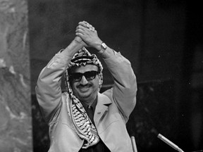 FILE - In this Nov. 13, 1974 file photo, Yasser Arafat clasps his arms over his head as he addresses the United Nations General Assembly, at U.N. headquarters. In 1974, Arafat was invited to represent the Palestine Liberation Organization and his people before the world body, where he made it clear he was ready to use any means for statehood. He spoke of oppressed people and liberation the world over. Wearing his trademark Palestinian keffiyeh scarf, he concluded with an enduring quote: "Today I have come bearing an olive branch and a freedom fighter's gun. Do not let the olive branch from my hand."