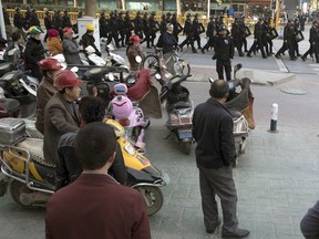 FILE - In this Nov. 5, 2017 file photo, residents watch a convoy of security personnel in a show of force through central Kashgar in western China's Xinjiang region. Two U.S. lawmakers are urging the extension of American export restrictions to prevent sales of equipment that could be used in China's massive security clampdown targeting the Xinjiang region's native Muslim population. Sen. Marco Rubio and Rep. Chris Smith said in a letter, Wednesday, Sept. 12, 2018, to the U.S. commerce secretary that they want foreign entities, including businesses, research institutions, government and private organizations, and individuals seen as profiting from the clampdown added to a watch list.