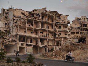 FILE - In this Sept. 20, 2018, file photo, motor cycles ride past buildings destroyed during the fighting in the northern town of Ariha in Idlib province, Syria. As world leaders talk peace at the U.N. this week, the Syrian region of Idlib clings to fragile hope that diplomacy will help avert a blowout battle over the country's last rebel stronghold.