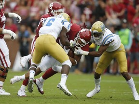 Oklahoma running back Rodney Anderson, center, is tackled by UCLA defensive back Adarius Pickett (6) and defensive back Quentin Lake (37) in the first quarter of an NCAA college football game in Norman, Okla., Saturday, Sept. 8, 2018.