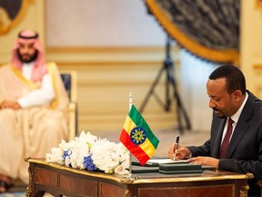In this photograph released by the state-run Saudi Press Agency, Ethiopian Prime Minister Abiy Ahmed, right, signs a peace accord with Eritrea as Saudi Crown Prince Mohammed bin Salman looks on in the distance in Jiddah, Saudi Arabia on Sunday, Sept. 16, 2018. The leaders of Ethiopia and Eritrea were in Saudi Arabia on Sunday to sign a peace accord between the two East African nations.